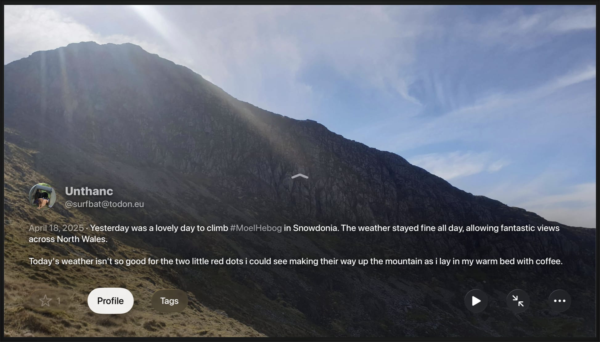 TV screen with a photo of a mountain. In the lower left corner is an image credit: Unthanc, @surfbat@todon.eu. Below that is a caption describing the photographer's experience, and buttons to mark the photo as a favorite, open the author's profile, open hashtags, play the slideshow, expand the image, and a menu of options.